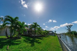 Un quartier résidentiel comprenant une maison, des palmiers, un quai et une étendue d’eau.