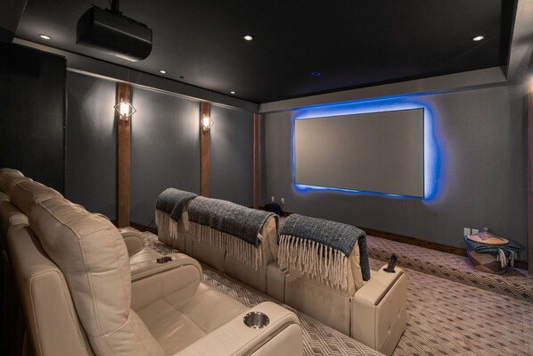 A home theater room with a large screen, comfortable seating, and a projector. - Mountain Escape | Hot Tub, Firepit, Movie Theatre + More! (Big Sky)