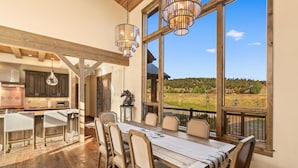 Comedor con una mesa grande y sillas, vigas de madera y vistas a un paisaje rural a través de amplios ventanales.