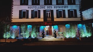 Un bâtiment sur lequel on peut lire l’inscription « HOSTELLERIE DES VOYAGEURS » et, sur un panneau plus petit, « Restaurant ».