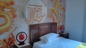 Une chambre d’hôtel avec un lit, une table de chevet, un mur décoratif orné d’un motif de dragon et une lampe rouge.