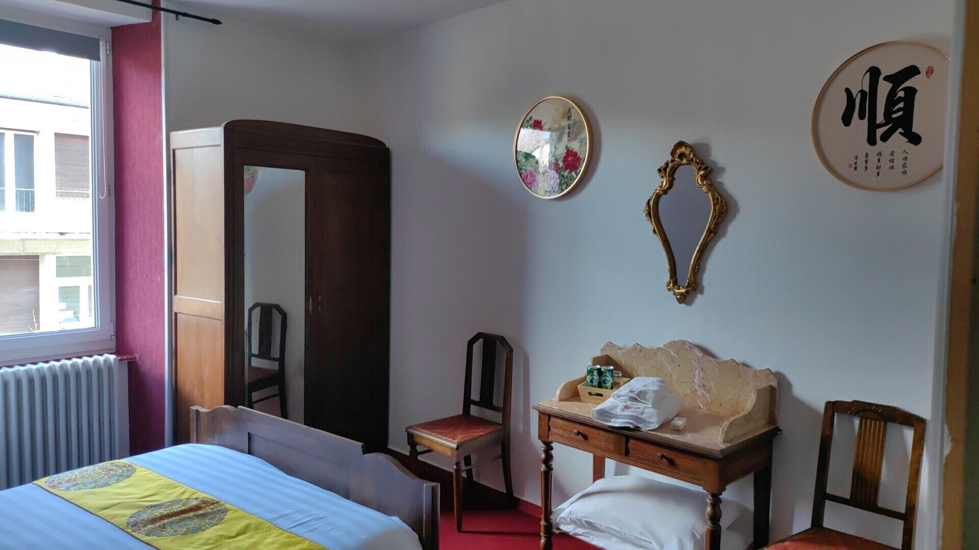 A hotel room with a bed, a wooden dresser, a mirror, and a wall with Chinese characters.