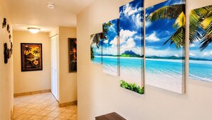 Um corredor com piso ladrilhado, uma porta e uma parede com arte tropical.