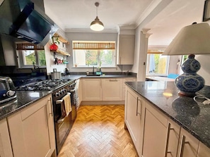 Une cuisine équipée d’une cuisinière, d’un four et d’un évier, avec un plancher en bois disposé en motif de parquet et une fenêtre avec des stores.