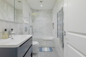 Un baño moderno con un tocador blanco, inodoro, ducha y un perchero para toallas.