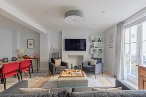 A modern living room with a sofa, chairs, a coffee table, a TV, and a dining area with a table and chairs.