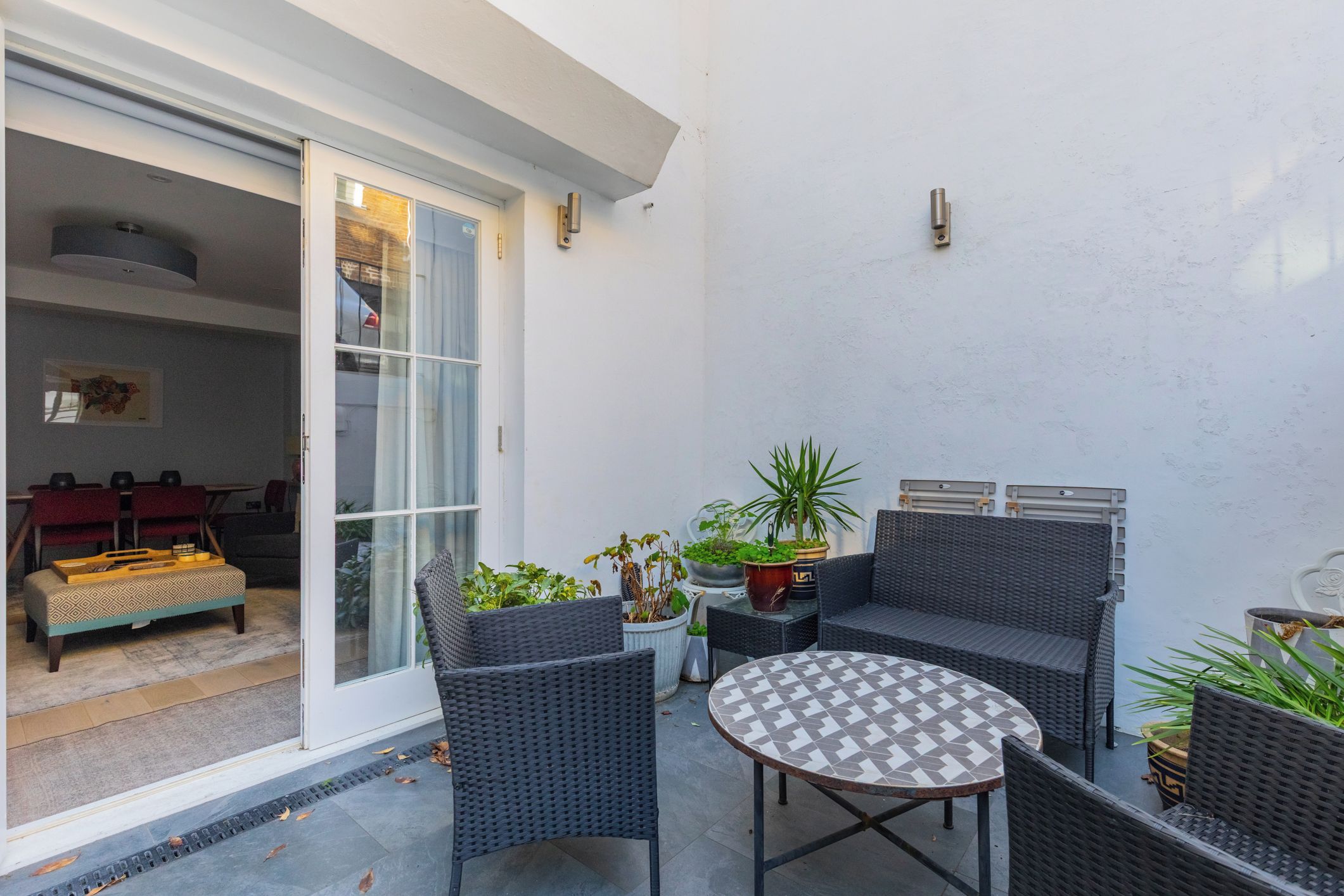 Eine Terrasse mit Korbmöbeln, einem runden Tisch und Blumentöpfen.