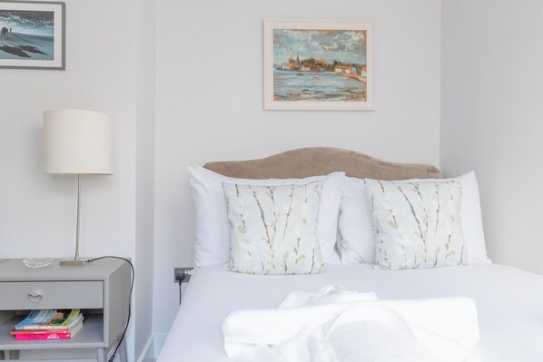 A hotel room with a bed, a nightstand, a lamp, and a painting on the wall.