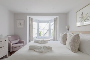 A hotel bedroom with a large bed, a sitting area with a chair, and a view of the outside.