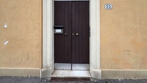 Una puerta de madera oscura con un picaporte de metal y un buzón, en una pared color crema con molduras blancas. Se ve el número '55' sobre la puerta.