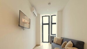 Una sala de estar moderna con un televisor de pantalla plana, un sofá con una manta y un cubo de basura.