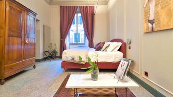 Une chambre avec une grande armoire en bois, un lit avec une literie rouge, une table blanche ornée d’un vase de fleurs et un tapis à motifs.