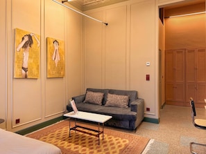 Ein Hotelzimmer mit einer grauen Couch, einem kleinen weißen Tisch, gemusterten Teppichen und zwei Bildern an der Wand.
