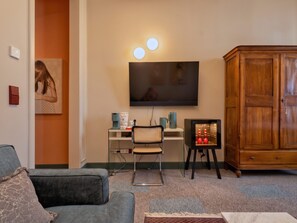 Ein Wohnzimmer mit Flachbildfernseher, einem Holzkasten, einem Schreibtisch mit Stuhl und einem Sofa.