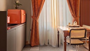 Habitación compacta con kitchenette, una mesa de comedor con sillas y una ventana con cortinas.