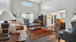 A spacious living room with a sofa, coffee table, and a TV. There is a dining area with chairs and a table.