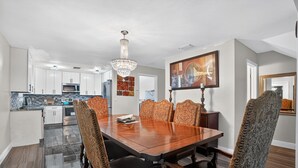 A dining area with a wooden table and ornate chairs, a chandelier, and a painting on the wall.