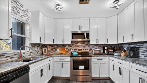 A modern kitchen with white cabinets, stainless steel appliances, and a tiled backsplash.