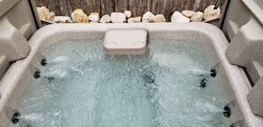 A hot tub with a beige cover, surrounded by rocks and a wooden fence. - Hideaway Cabin 3 Bedroom Cabin (Uvalde)