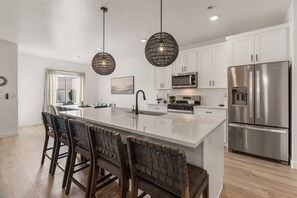 Een moderne keuken met een centraal eiland, roestvrijstalen apparatuur en hanglampen.