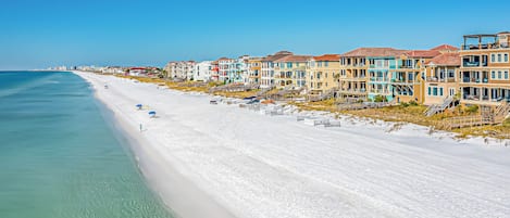 A beachfront hotel with multiple-story buildings, a sandy beach, and clear blue waters.