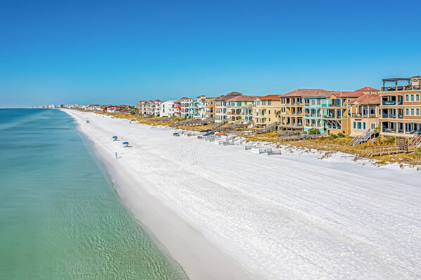 A beachfront hotel with multiple-story buildings, a sandy beach, and clear blue waters.
