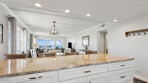 A spacious kitchen with a large granite countertop, white cabinetry, and a hanging light fixture.