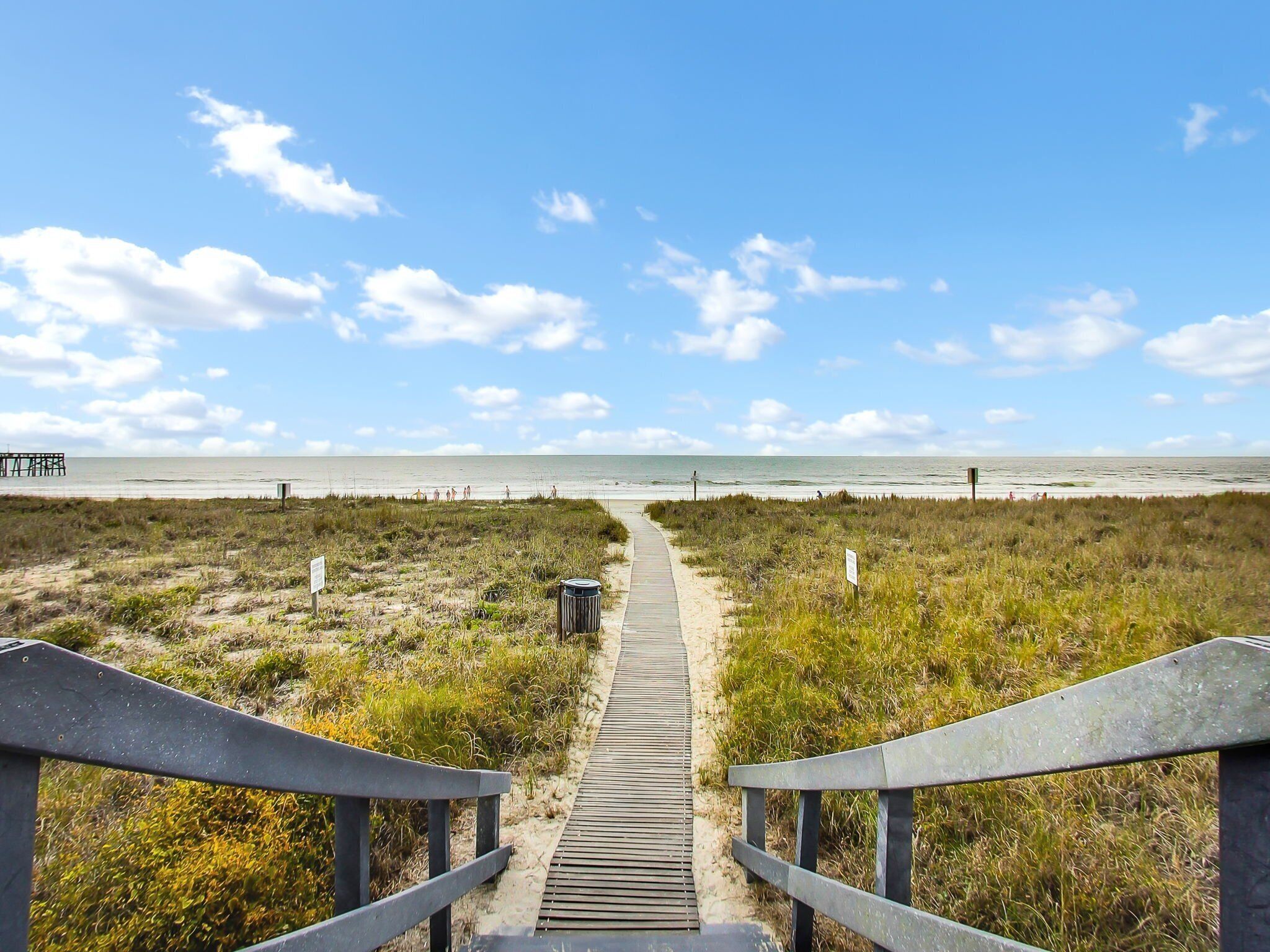A wooden boardwalk leading to a beach with a clear sky.