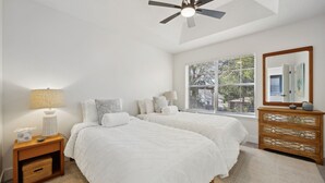 A bedroom with two beds, a nightstand, a dresser, a ceiling fan, and a window with blinds. - 322 S. 5th Street Unit A 3 Bedroom Townhouse (Fernandina Beach)