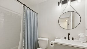 A bathroom with a white toilet, a sink with a mirror, and a shower curtain. - 322 S. 5th Street Unit A 3 Bedroom Townhouse (Fernandina Beach)