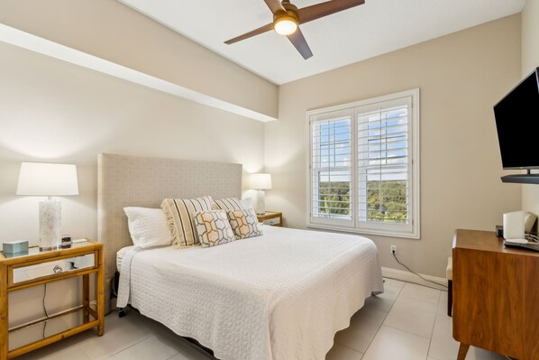 A bedroom with a bed, nightstands, a desk, a ceiling fan, and a window with blinds. - 21 Ocean Place 3 Bedroom Condo (Fernandina Beach)