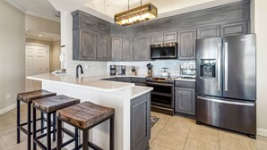 A modern kitchen with dark cabinets, a stainless steel refrigerator, a built-in oven, and a central island with stools.