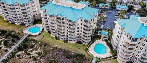A high-rise hotel with multiple balconies, a swimming pool, and a parking area.