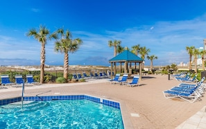A pool area with lounge chairs, a gazebo, and palm trees.