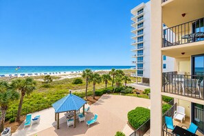 A beachfront view from a hotel balcony overlooking a sandy beach with umbrellas and lounge chairs.