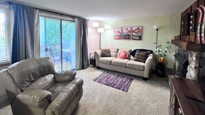 Un salon avec un canapé en cuir, un divan beige et un tapis à rayures. Une porte-fenêtre coulissante donne accès à un balcon.