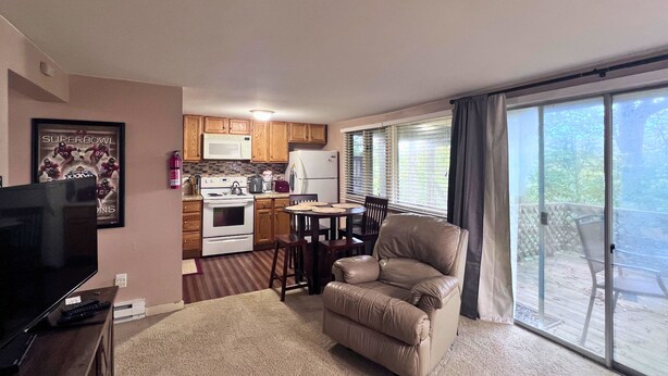 Un salon avec un téléviseur, un canapé beige, une cuisine avec des meubles en bois et une cuisinière, et un balcon avec vue.