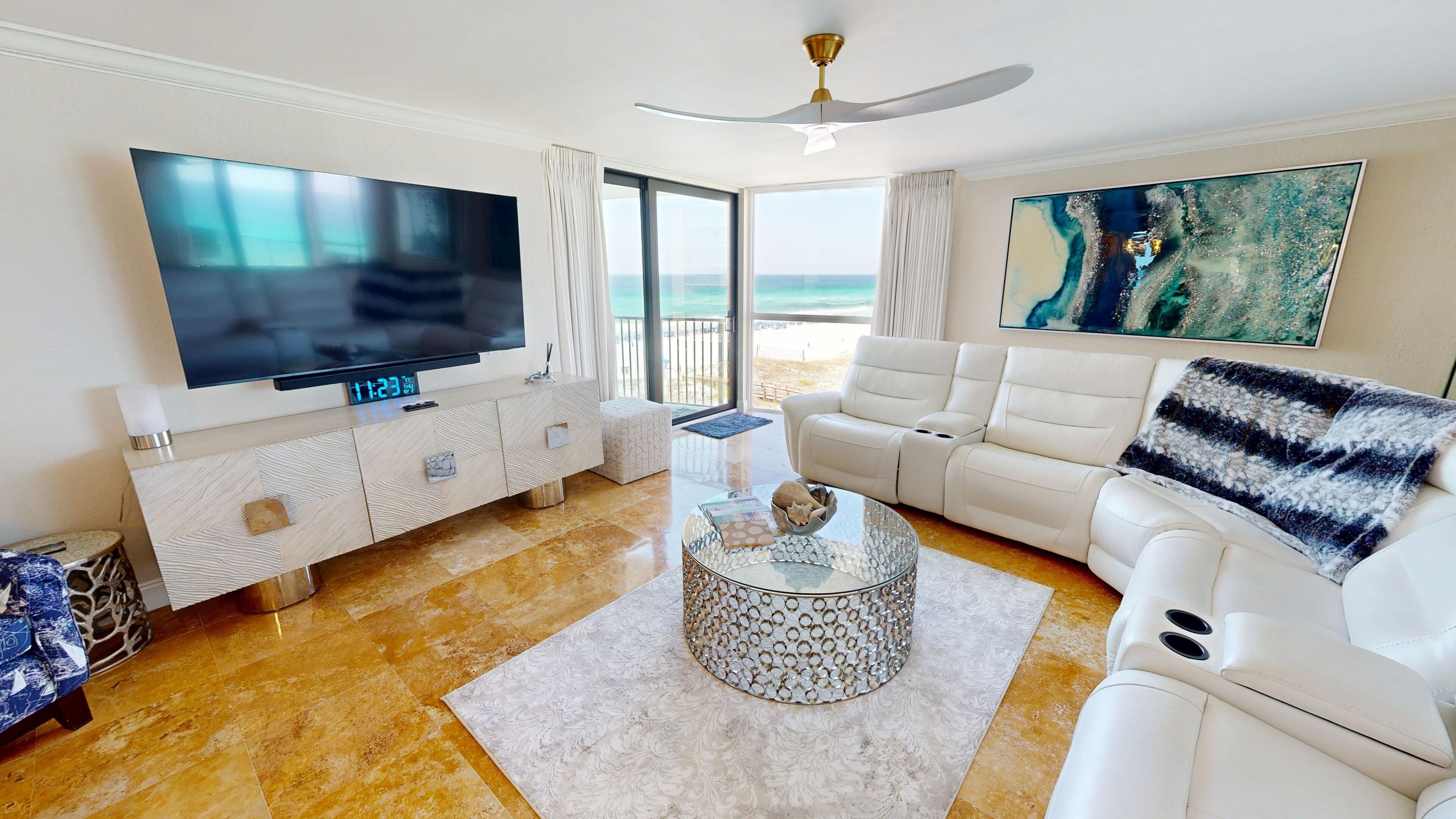 A modern living room with a flat-screen TV, a sofa, a coffee table, and a view of the ocean.