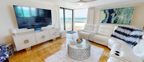 A modern living room with a flat-screen TV, a sofa, a coffee table, and a view of the ocean.