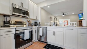 A modern kitchen with white cabinets, stainless steel appliances, and a tiled floor.
