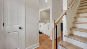 A clean, modern kitchen with white cabinets and a wooden staircase.