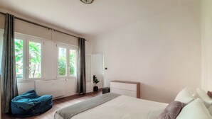 A bedroom with a large bed, a blue bean bag, a bedside table, and a view of greenery outside. - Como Gateway (Como)