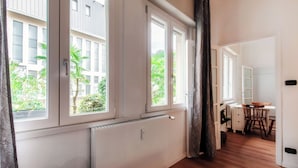 A room with large windows, a radiator, a wooden floor, and a dining area with chairs and a table. - Como Gateway (Como)