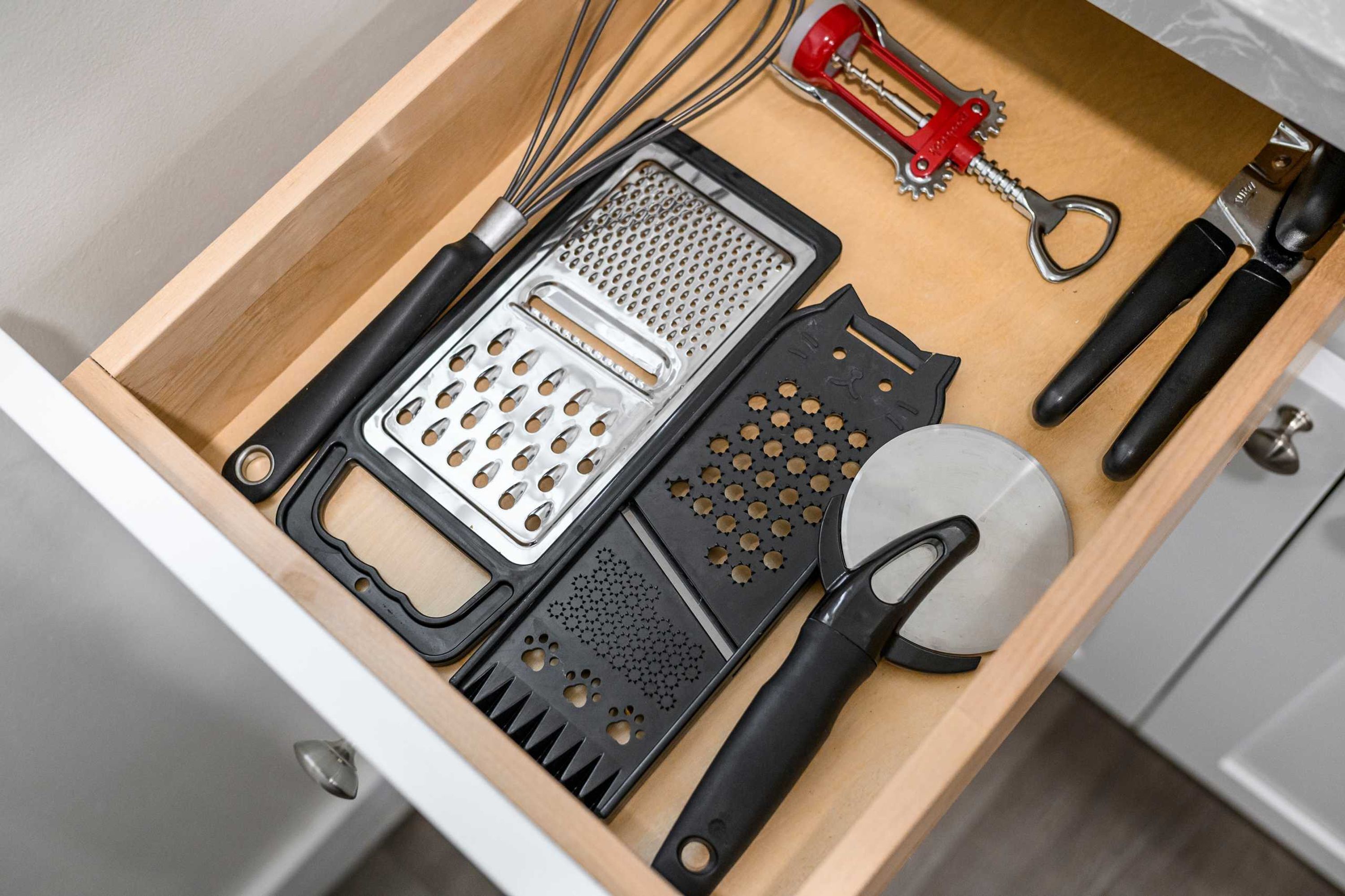 A drawer with various kitchen tools including a grater, a grater with holes, a grater with a handle, a grater with a hole pattern, and a grater with a handle and holes.