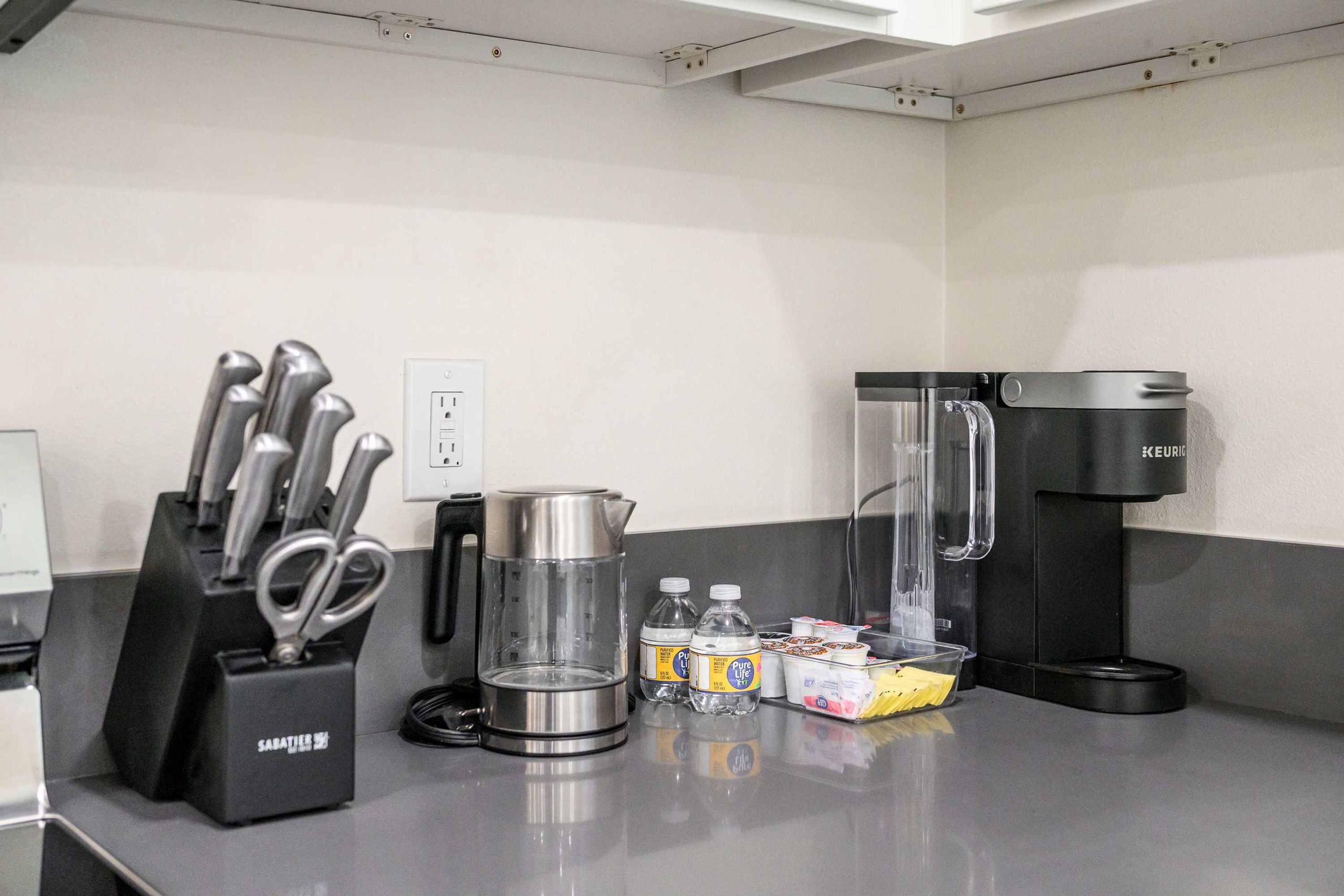 A kitchenette with a coffee maker, a kettle, a water dispenser, and a knife block.