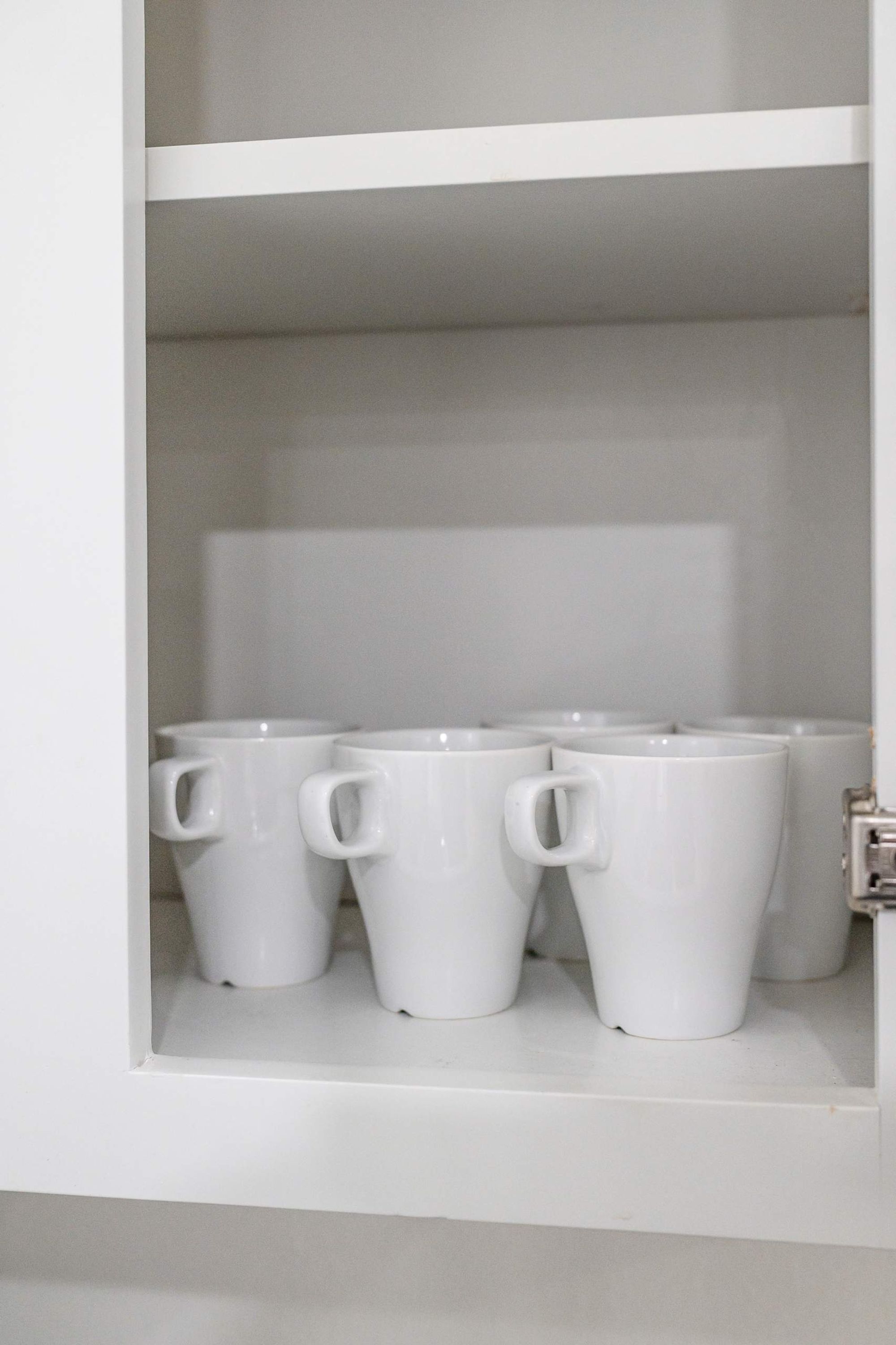 Un mueble blanco con varias tazas blancas dispuestas en los estantes.
