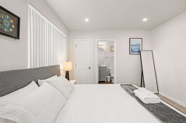 A hotel room with a bed, a bedside lamp, a framed artwork on the wall, a standing mirror, and a view into the bathroom. - Stylish Home w Free Parking Near LA Hotspots 8 (Altadena)