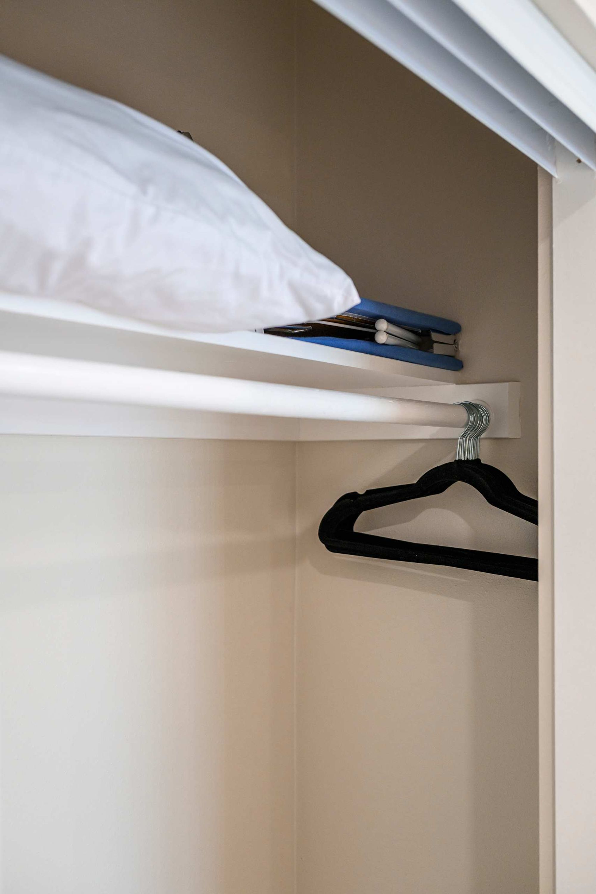 A bunk bed with a white mattress and a shelf above it holding a book and a blue object.