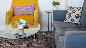 A living room with a yellow armchair, a grey sofa, a small table with a glass top, a framed picture on the wall, and a potted plant. - Stylish Home w Free Parking Near LA Hotspots 8 (Altadena)