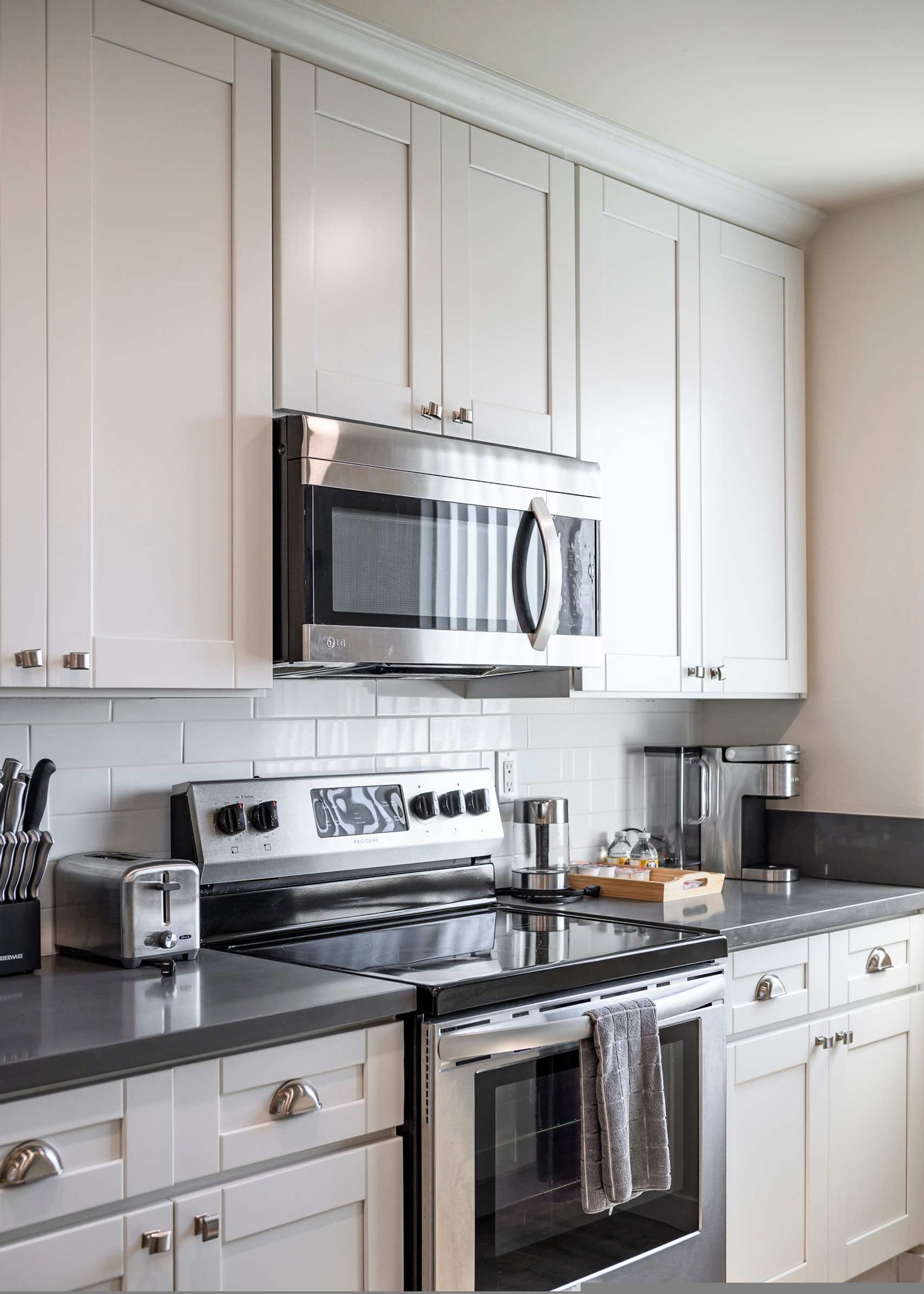A kitchen with white cabinets, a stainless steel microwave, a stove, and a toaster.